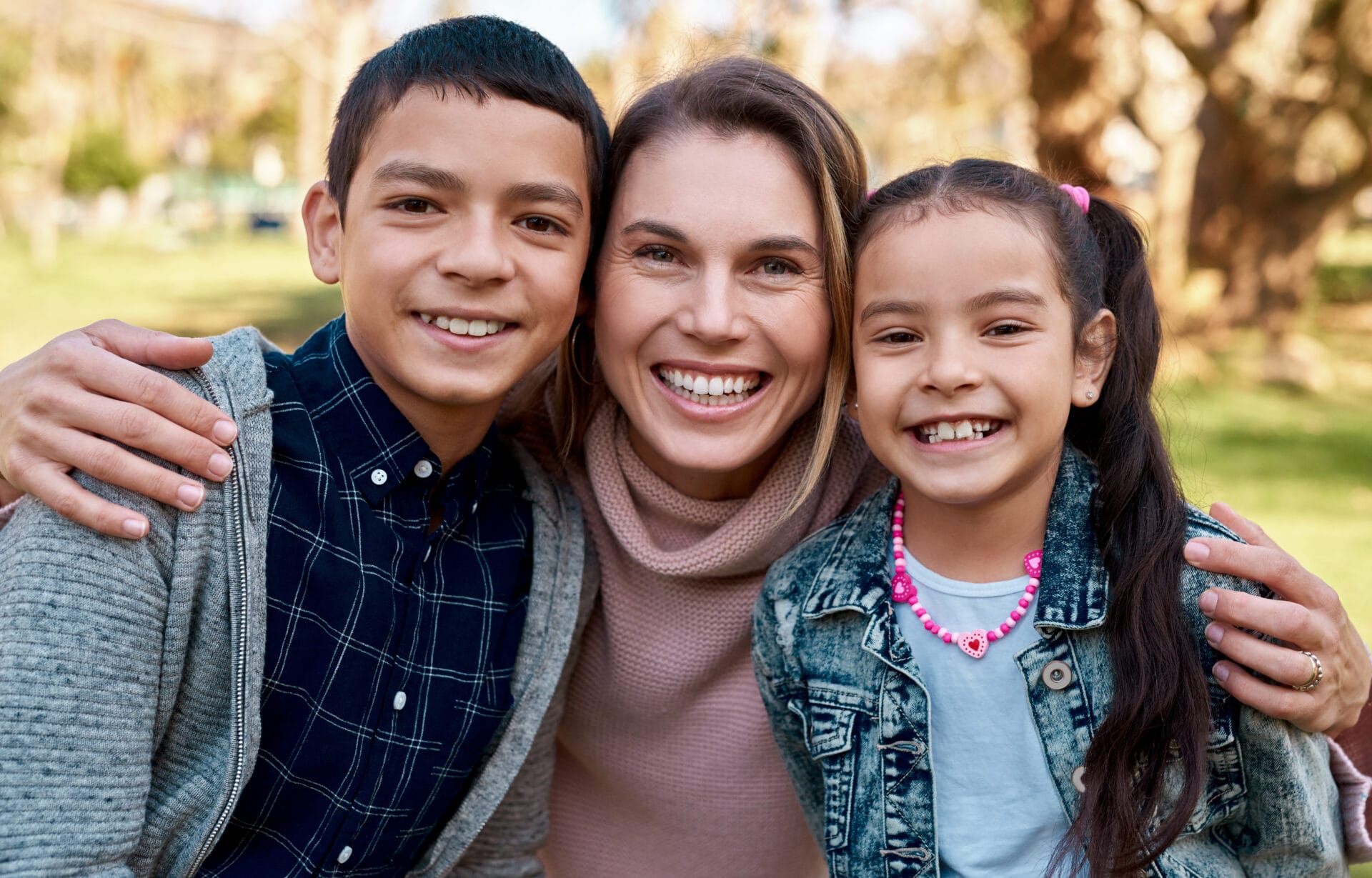 Woman smiling with her arms wrapped around two children by her side.
